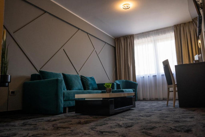 Zonă lounge cu canapea din catifea verde, măsuță neagră cu plantă, birou și scaun lângă fereastră.