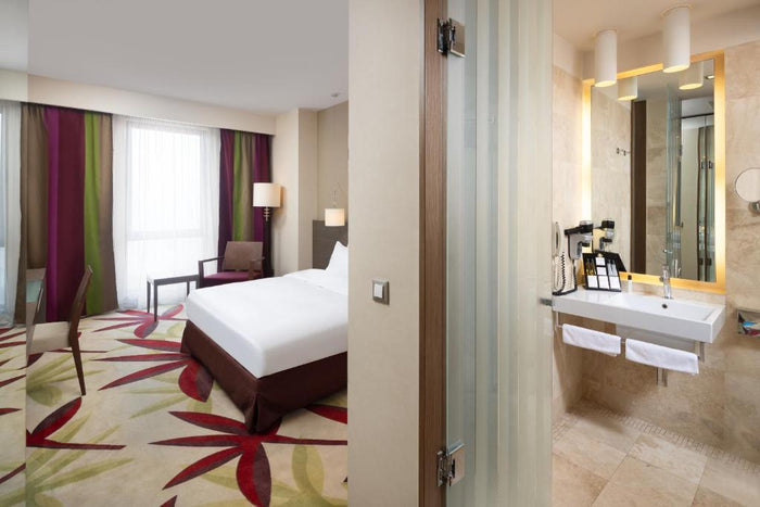 Cameră dublă la Golden Tulip Cluj-Napoca, cu mochetă cu frunze roșii și verzi, draperii colorate și baia alăturată.