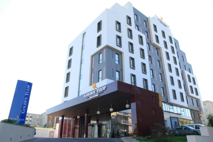 Fațada hotelului Golden Tulip Ana Dome din Cluj-Napoca, fotografiată ziua, cu copertina și totemul de la intrare.