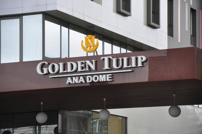 Firma de la intrarea hotelului Golden Tulip Ana Dome, cu sigla lalelei aurii și lustre sferice sub copertină.