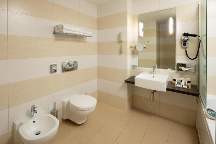 Baie la Golden Tulip Sibiu, cu toaletă și bideu suspendate, lavoar pe blat și uscător de păr pe perete.