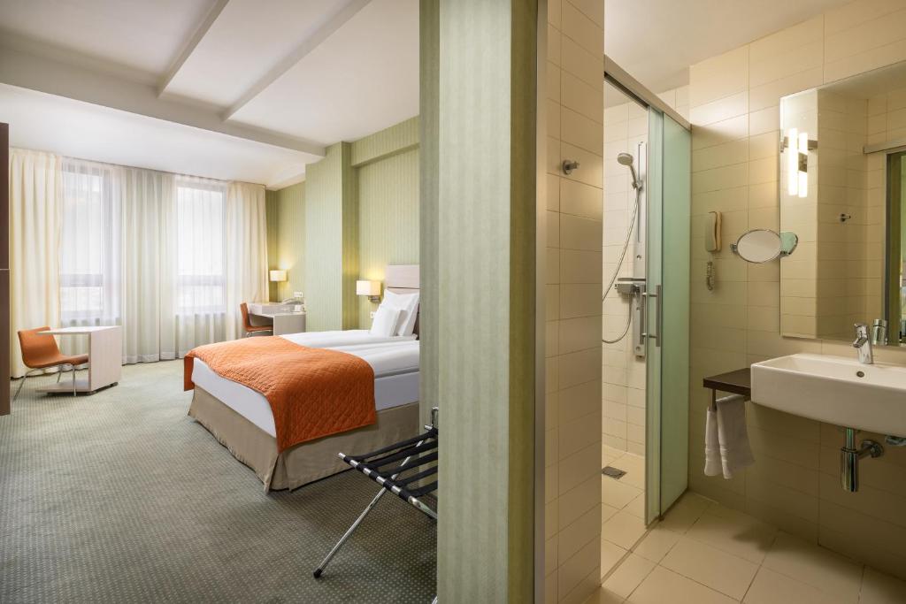 Cameră la Golden Tulip Sibiu, cu cuvertură portocalie pe pat, birou cu scaun portocaliu și baia alăturată.