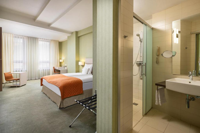 Cameră la Golden Tulip Sibiu, cu cuvertură portocalie pe pat, birou cu scaun portocaliu și baia alăturată.