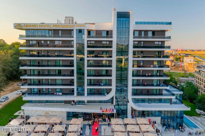 Vedere aeriană a Grand Hotel President la amurg, cu intrarea cu covor roșu, terase și piscină laterală.