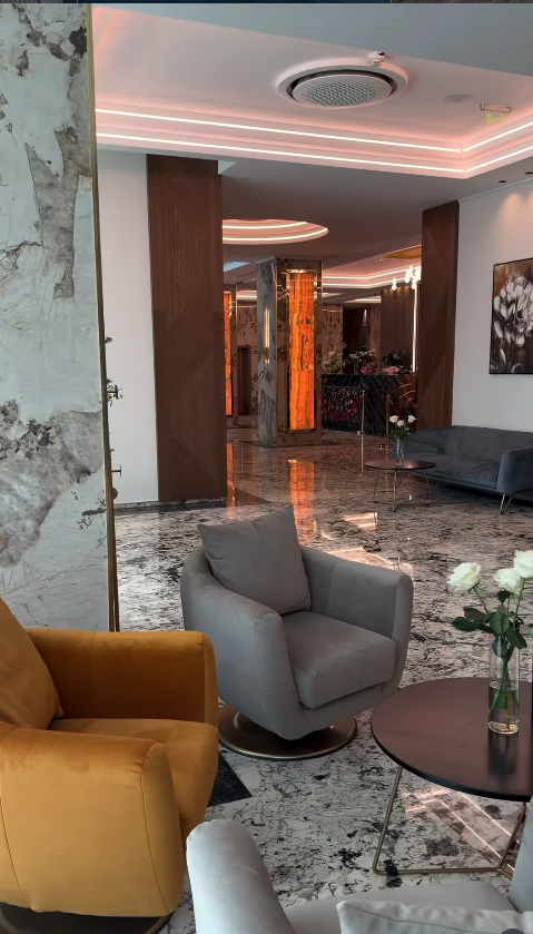 Zonă de lounge cu fotoliu muștar și fotoliu gri pe podea din marmură, măsuță cu trandafiri și canapea gri.