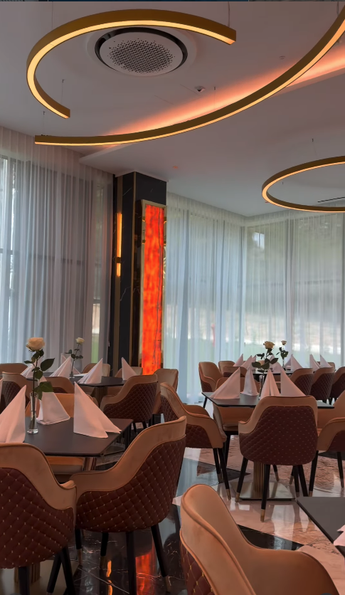 Sală de restaurant cu două lustre circulare aurii suspendate deasupra meselor pregătite cu trandafiri.