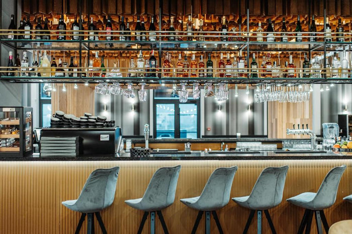 Raft de bar din sticlă și metal, plin cu sticle, pahare agățate deasupra blatului și espressor profesional.