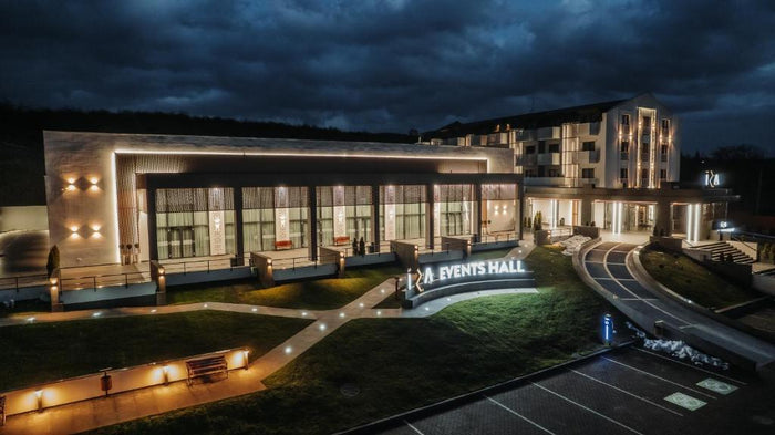 Corpul de evenimente iluminat seara, cu ferestre înalte și literele Events Hall montate pe zidul curbat.