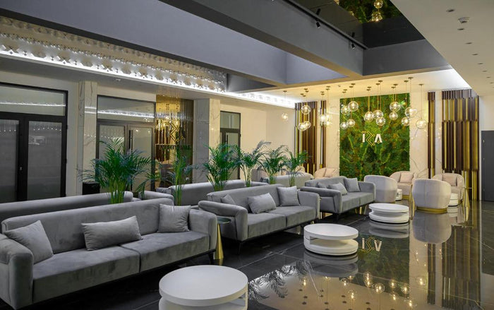 Lounge cu șiruri de canapele gri, măsuțe rotunde albe, palmieri și perete vegetal cu sigla hotelului.