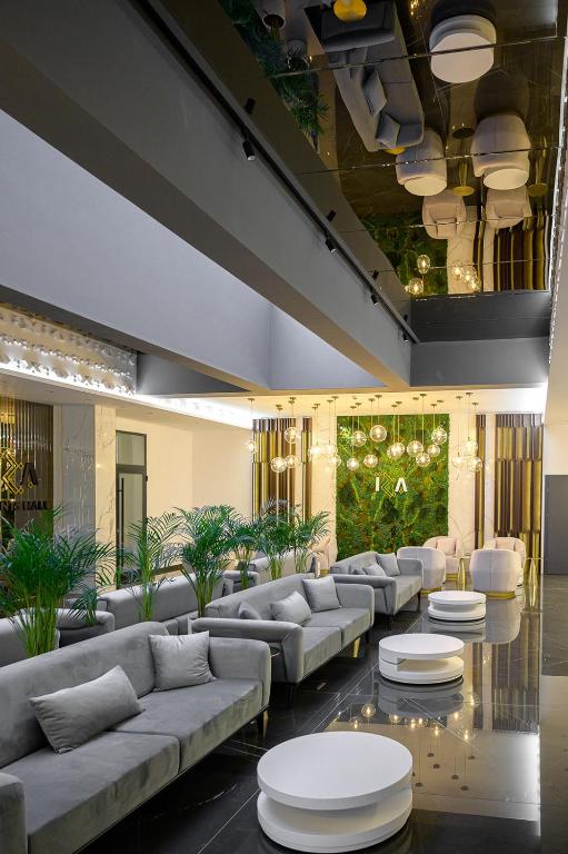 Lounge fotografiat pe verticală, cu tavan-oglindă care reflectă canapelele gri și palmierii de la parter.