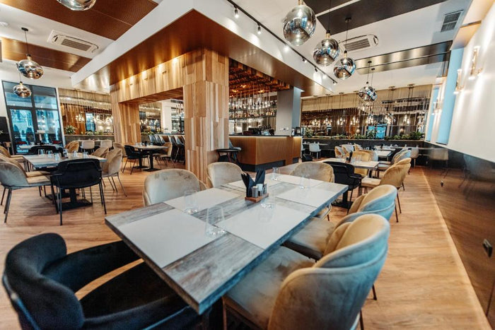 Restaurant cu pendule sferice cromate, mese pregătite cu suporturi albe și scaune din catifea crem și gri.