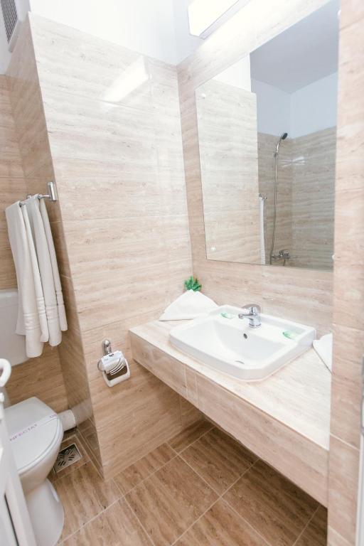 Baie la Hotel Mureș, placată cu travertin bej, cu lavoar pe blat, oglindă mare, prosop alb și săpunuri verzi.