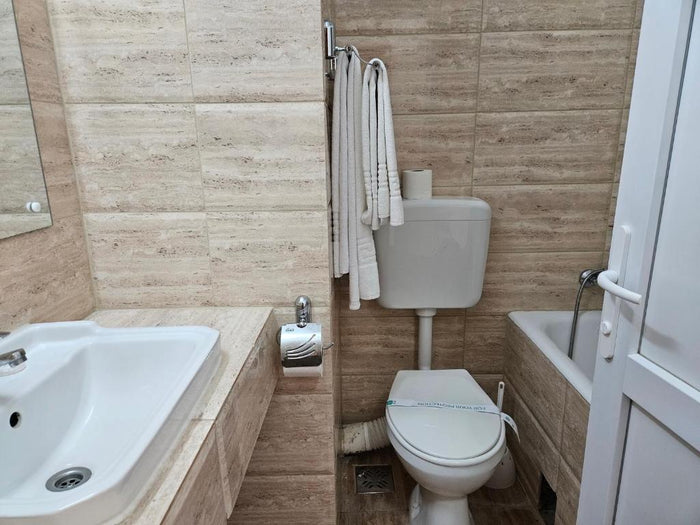 Baie la Hotel Mureș, cu toaletă cu rezervor montat pe perete, cadă, lavoar și prosoape albe pe suport.