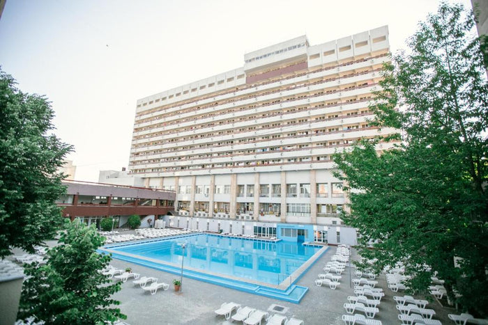 Piscină exterioară cu șezlonguri albe la Băile Felix, în fața unui corp de hotel cu balcoane pe mai multe etaje.