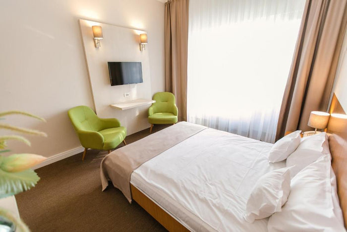 Cameră la Hotel Nufărul, cu pat matrimonial, două fotolii verzi și televizor montat pe panoul alb de perete.
