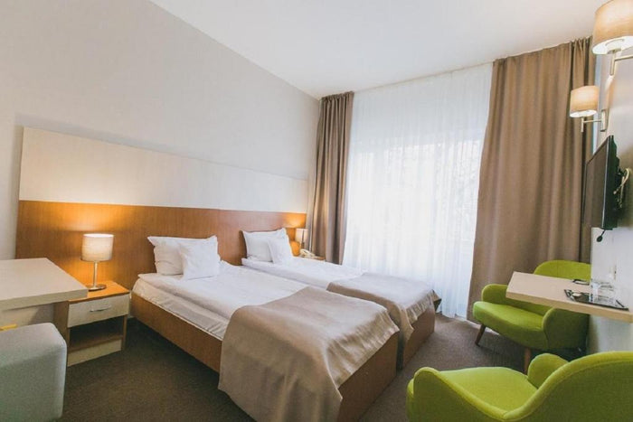 Cameră twin la Hotel Nufărul, cu fereastră mare cu perdea și draperie taupe, fotolii verzi, birou și televizor.