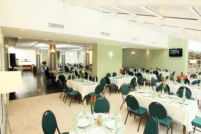 Sala de restaurant a Hotel Nufărul, cu scaune tapițate verde, fețe de masă albe și pardoseală din lemn deschis.