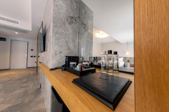 Colț de bar din cameră la Hotel One, cu aparat de cafea, sticle de apă personalizate și mapă din piele.