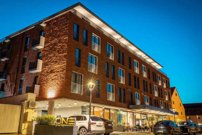 Fațada din cărămidă a Hotel One Alba Iulia, fotografiată seara, cu terasa restaurantului luminată la parter.