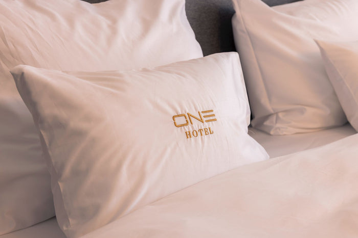 Detaliu al lenjeriei de pat personalizate de la Hotel One, cu sigla ONE Hotel brodată în fir auriu.