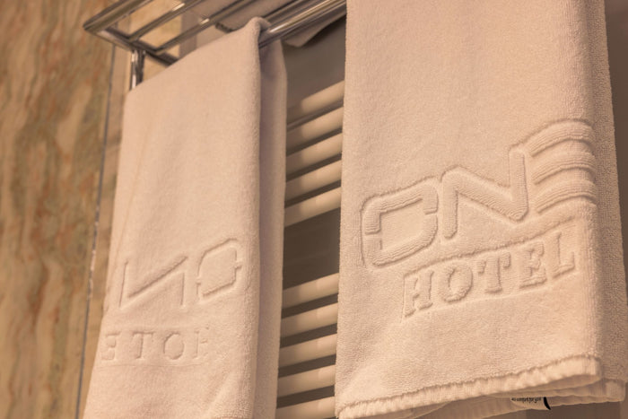 Detaliu al unui prosop jaquard personalizat de la Hotel One, cu sigla ONE Hotel țesută în material.
