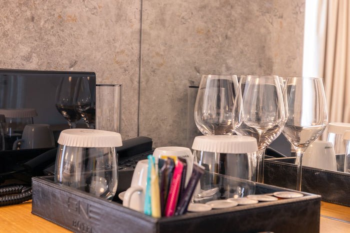 Tavă de cameră la Hotel One cu pahare de vin, capsule de cafea și articole de minibar, pe blatul din lemn.
