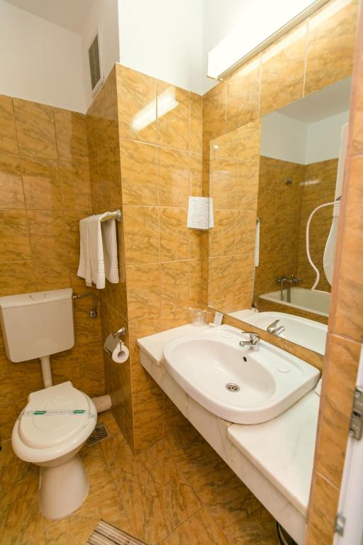 Baie placată cu faianță ocru la Hotel Poienița, cu lavoar pe blat de marmură, oglindă mare și prosoape albe pe suport.