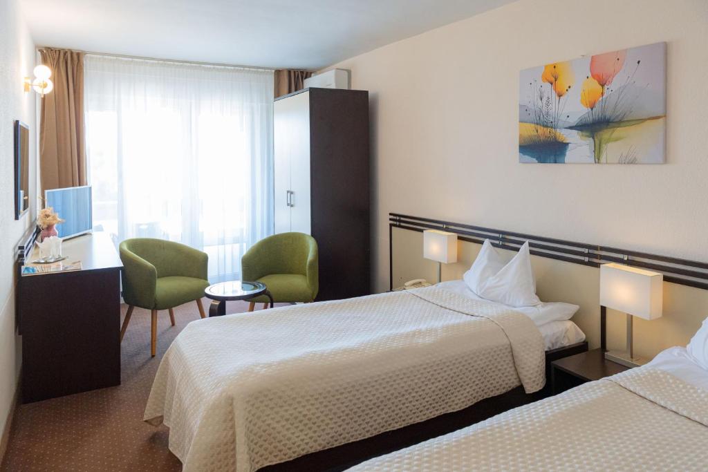 Cameră dublă la Hotel Poienița, cu două paturi, fotolii verzi lângă fereastră, birou și dulap închis la culoare.