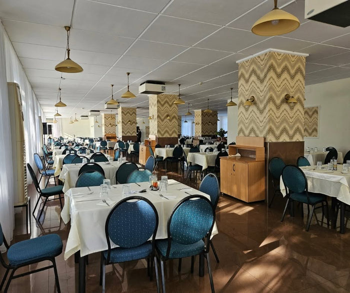 Sala de mese a Hotel Poienița, cu scaune tapițate în albastru-petrol, fețe de masă albe și lustre cu abajur auriu.