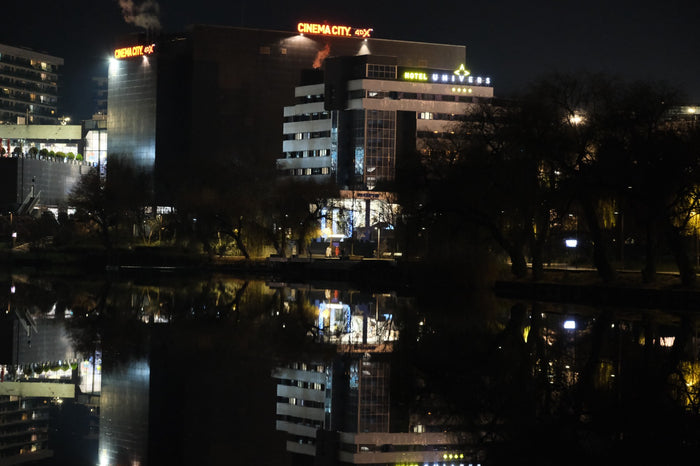 Clădirea hotelului cu firma luminoasă, văzută noaptea de peste lac, cu luminile orașului oglindite în apă.