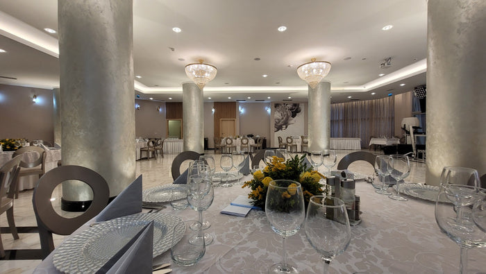 Sală de restaurant cu coloane placate argintiu, candelabre de cristal și mese aranjate cu fețe albe.