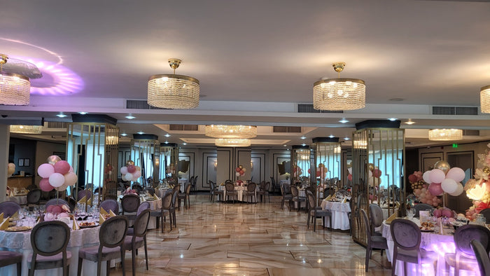 Sală de evenimente cu candelabre de cristal, paravane aurii cu oglinzi, mese rotunde și scaune tip medalion.
