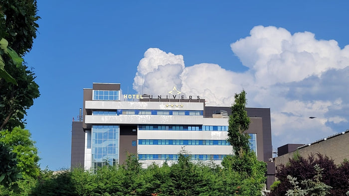 Sigla luminoasă HOTEL UNIVERS cu patru stele, montată pe aticul clădirii, pe fundal de cer albastru cu nori.