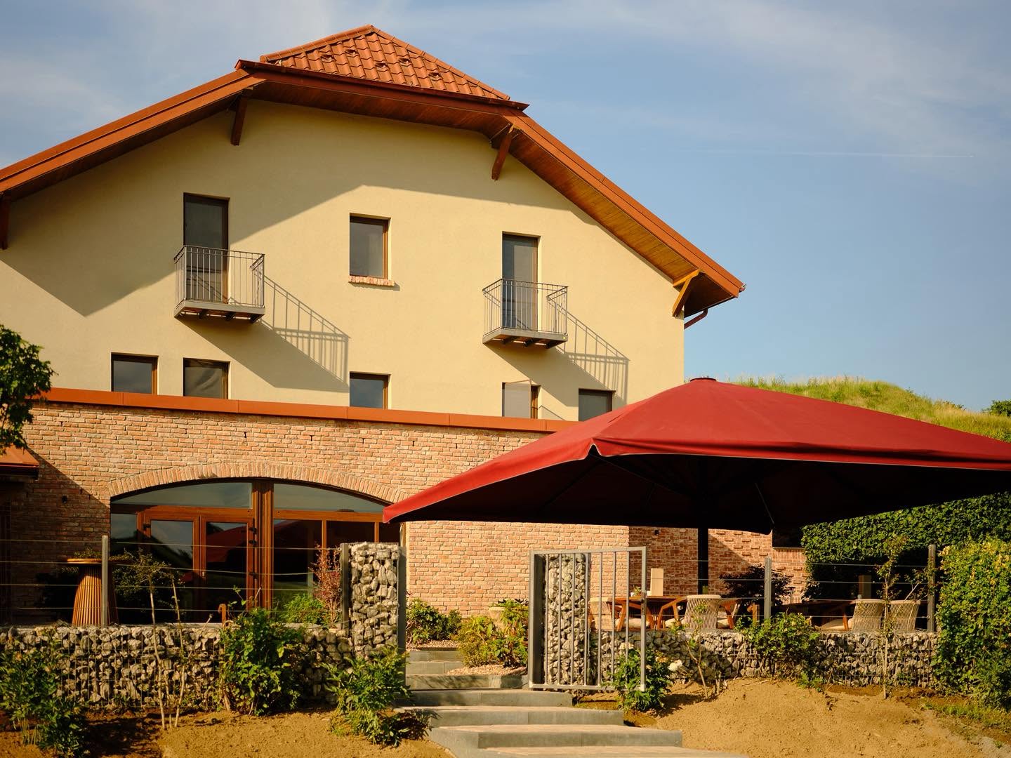 Clădirea Issa Garden din Turda, cu parter din cărămidă, balcoane la etaj și terasă sub o umbrelă roșie.