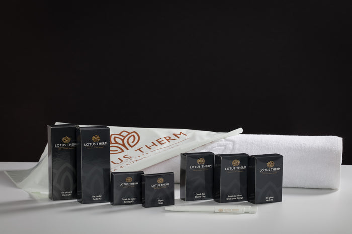 Set de amenities Lotus Therm — seturi de bărbierit, dentar, cusut, șapcă de duș — aranjate cu un prosop pe fundal negru.