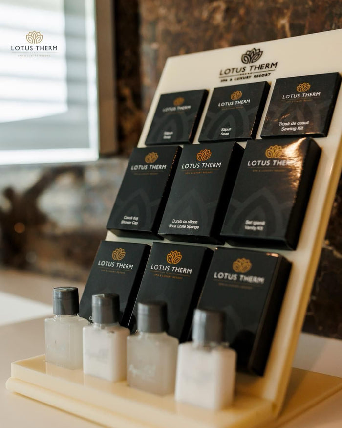 Suport înclinat cu amenities personalizate Lotus Therm — săpunuri, trusă de cusut și sticluțe cosmetice — lângă fereastră.