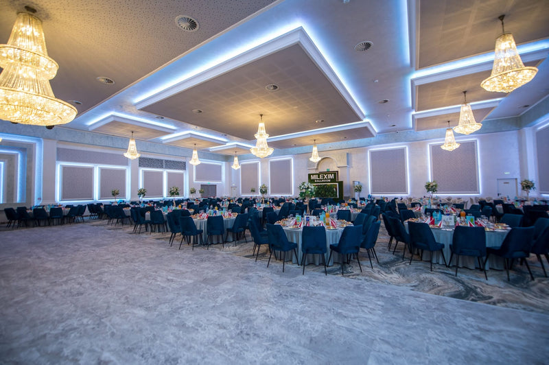 Sala Milexim Ballroom cu mese rotunde pregătite, scaune din catifea bleumarin și candelabre mari de cristal.