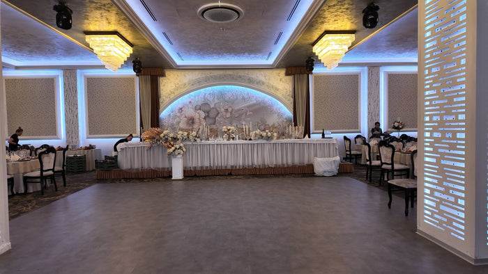 Masa prezidiului îmbrăcată în alb, în fața unui decor floral în arcadă, cu ringul de dans liber în prim-plan.