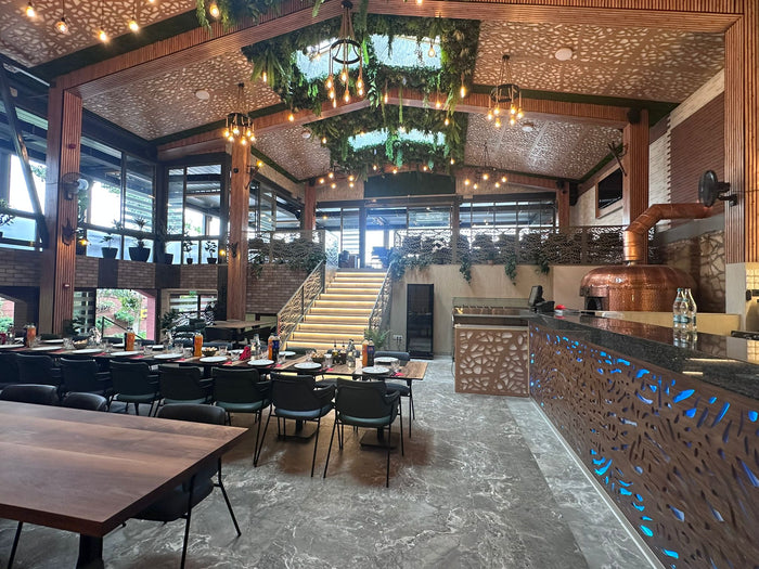 Sala restaurantului cu plafon vegetal și becuri decorative, cazan de cupru și bar cu front decupat iluminat.