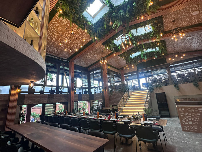 Interiorul restaurantului cu scară iluminată, luminator în tavan, plante suspendate și mese lungi din lemn.