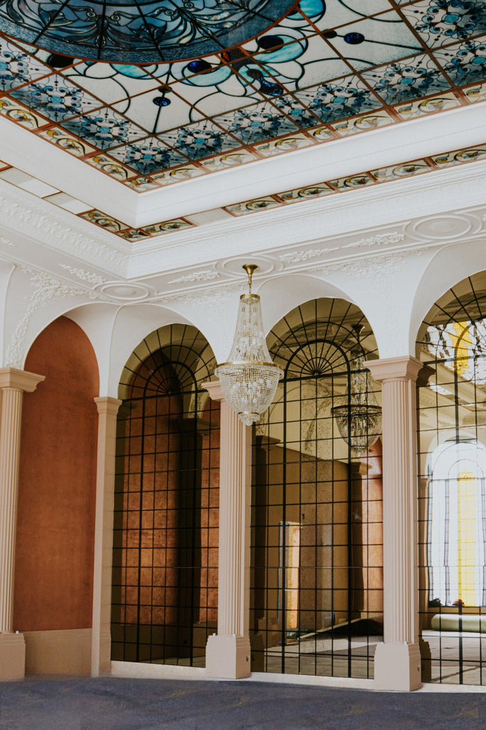 Colț de sală cu arcade din sticlă, tavan cu vitralii albastre și un candelabru din cristal suspendat.