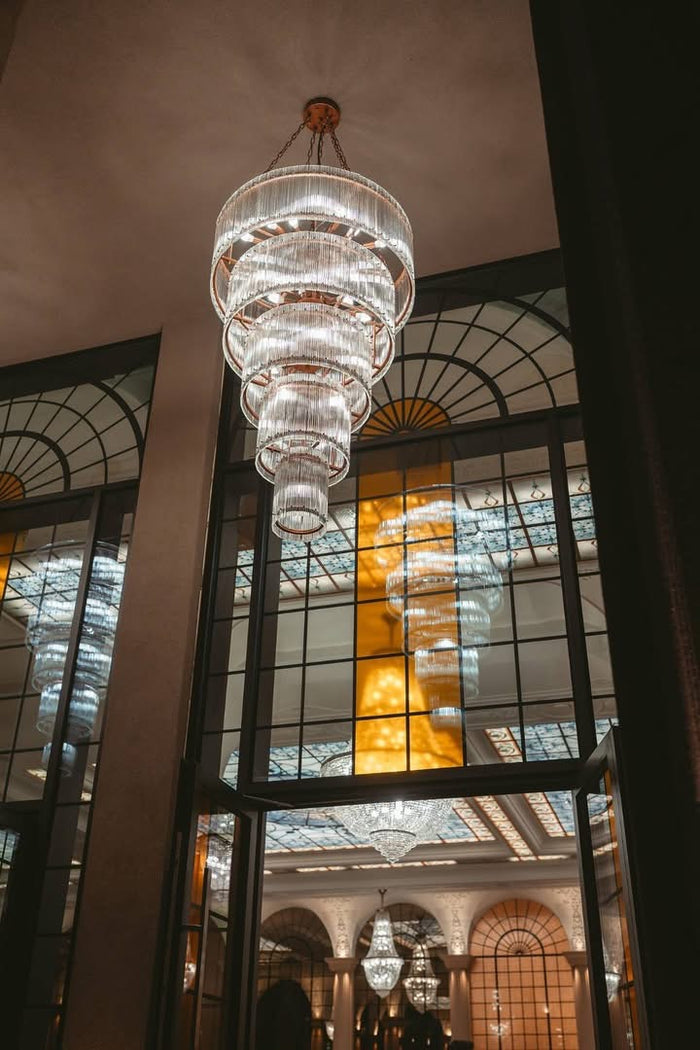 Vedere din pragul unei uși din sticlă spre un candelabru etajat, cu reflexii în panourile vecine din sticlă.