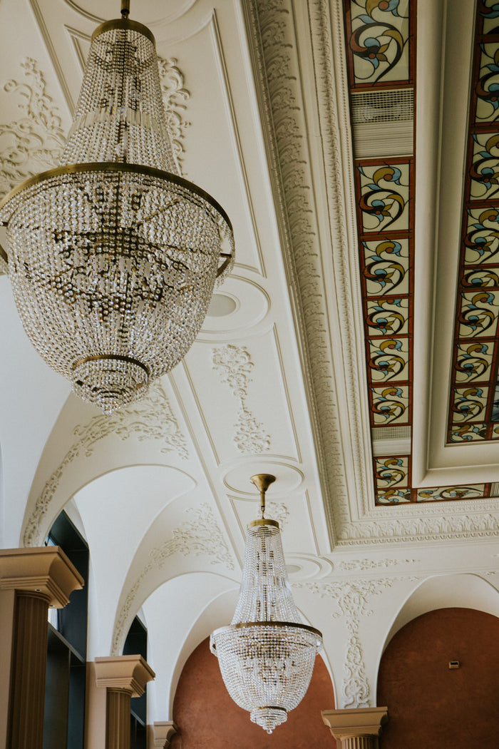 Coridor boltit cu două candelabre din cristal, arcade și nișe teracotă sub un tavan cu vitralii colorate.