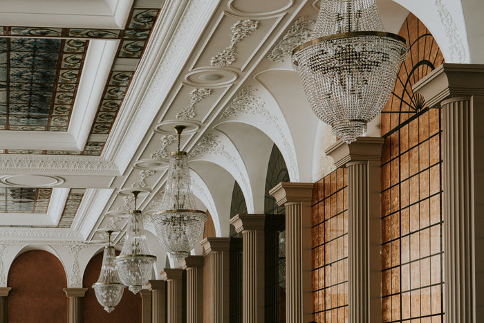Șir de candelabre din cristal de-a lungul unei galerii cu coloane și pereți din sticlă în nuanțe aurii.