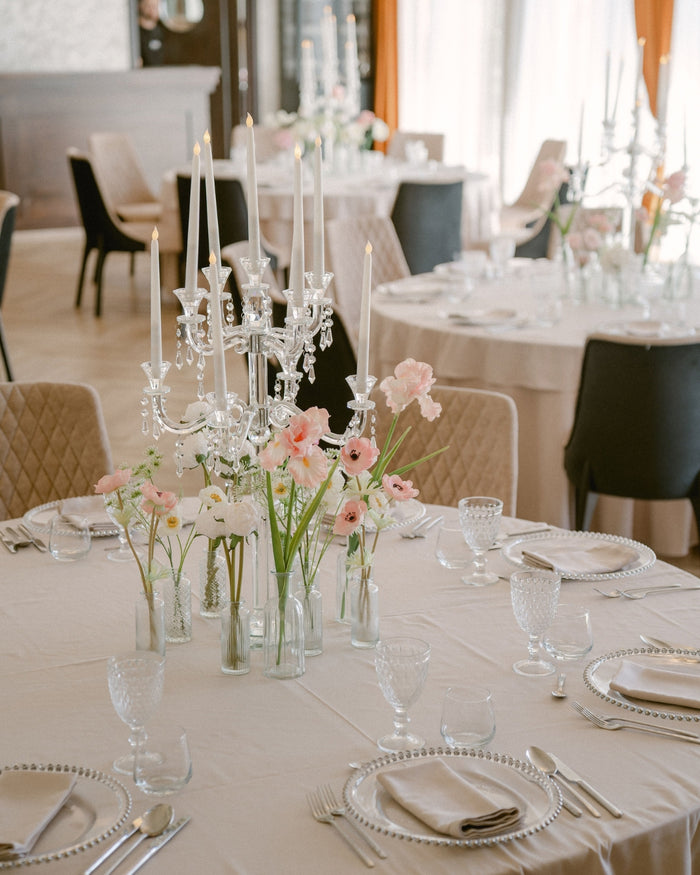 Candelabru din cristal cu lumânări aprinse, alături de un aranjament floral roz și alb pe masa de eveniment.
