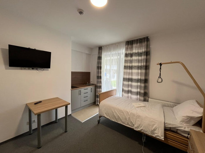 Cameră individuală cu chicinetă la Cluj Senior Village, cu pat de îngrijire, mobilier și draperii.