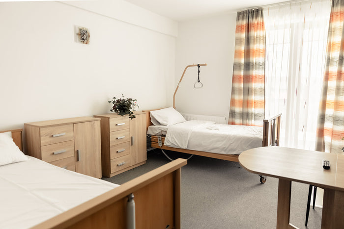 Cameră de rezidenți la Cluj Senior Village, cu paturi de îngrijire, mobilier și draperii.