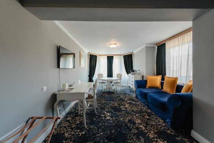 Livingul unui apartament, cu canapea albastră și perne muștar, birou alb, masă rotundă și mochetă florală.
