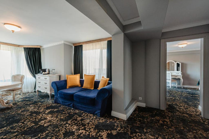 Apartament cu două încăperi: canapea albastră și comodă albă în living, iar prin ușă se vede masa de toaletă.