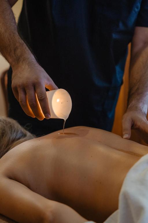 Masaj cu ulei cald turnat dintr-o cupă de ceramică, într-o cabină de tratament luminată discret.